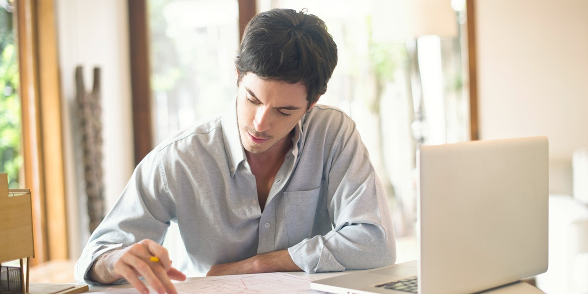 man reading physical document next to a laptop