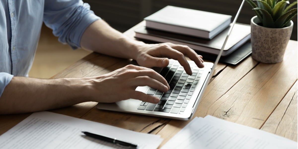 close up of a man's hands typing on a laptop