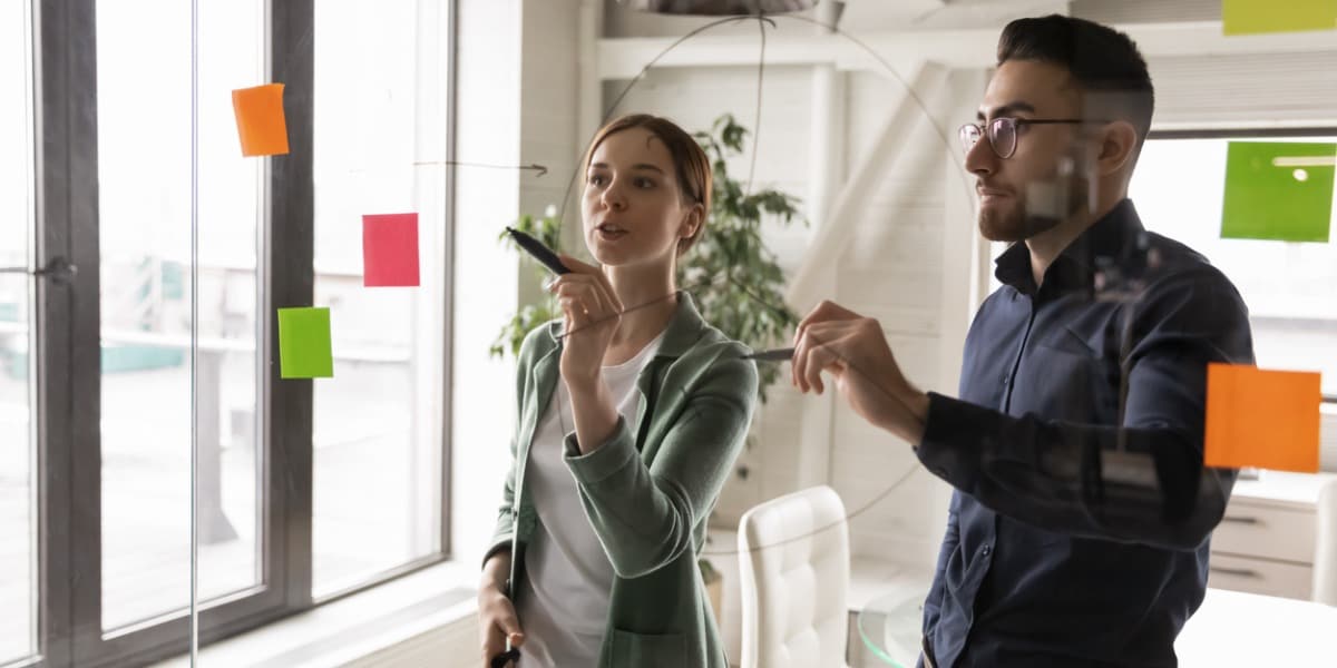 coworkers discussing ideas near a glass wall with sticky notes