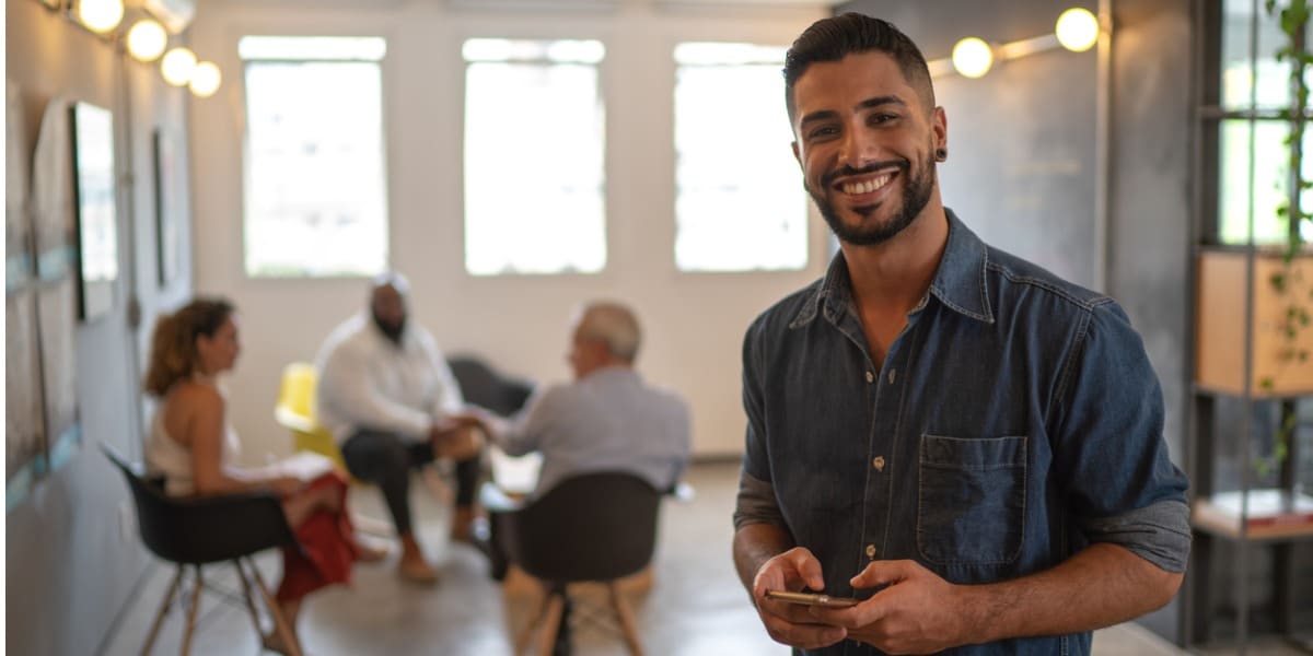 latin man smiling, people working in the background