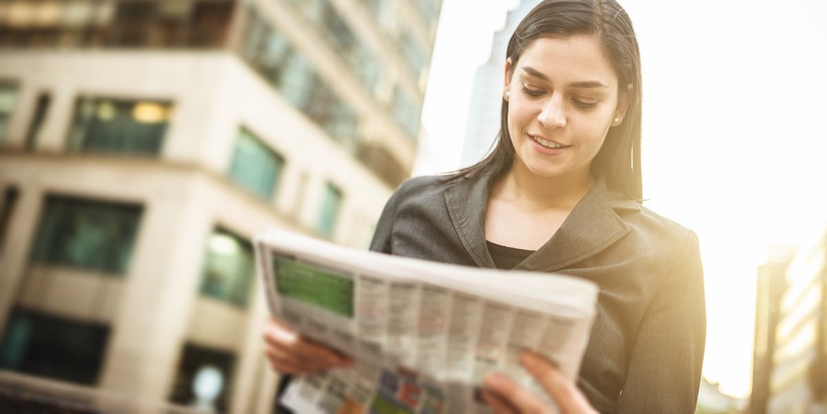 mujer leyendo periodico afuera, ciudad