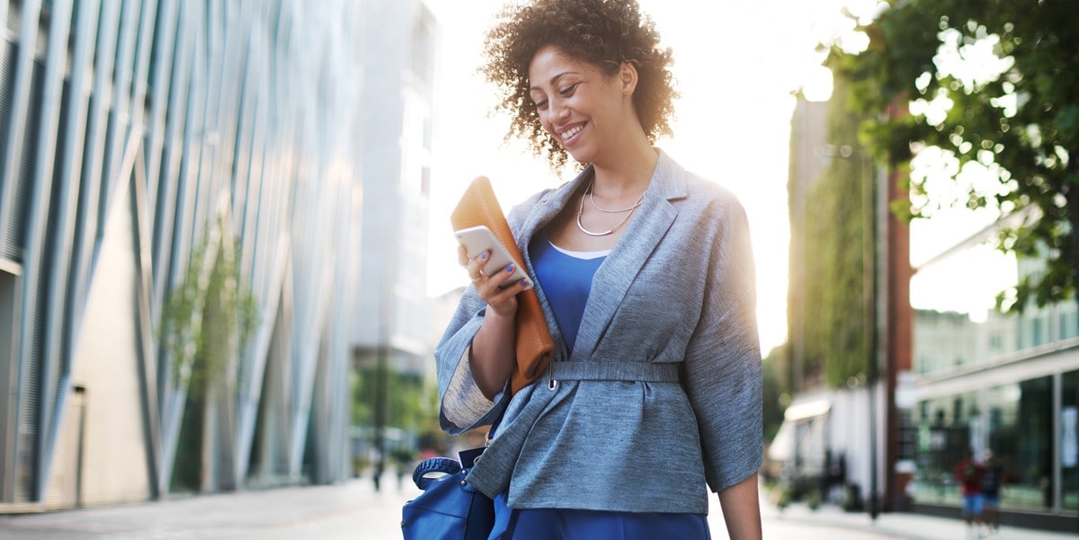 mujer caminando afuera con celular y equipaje