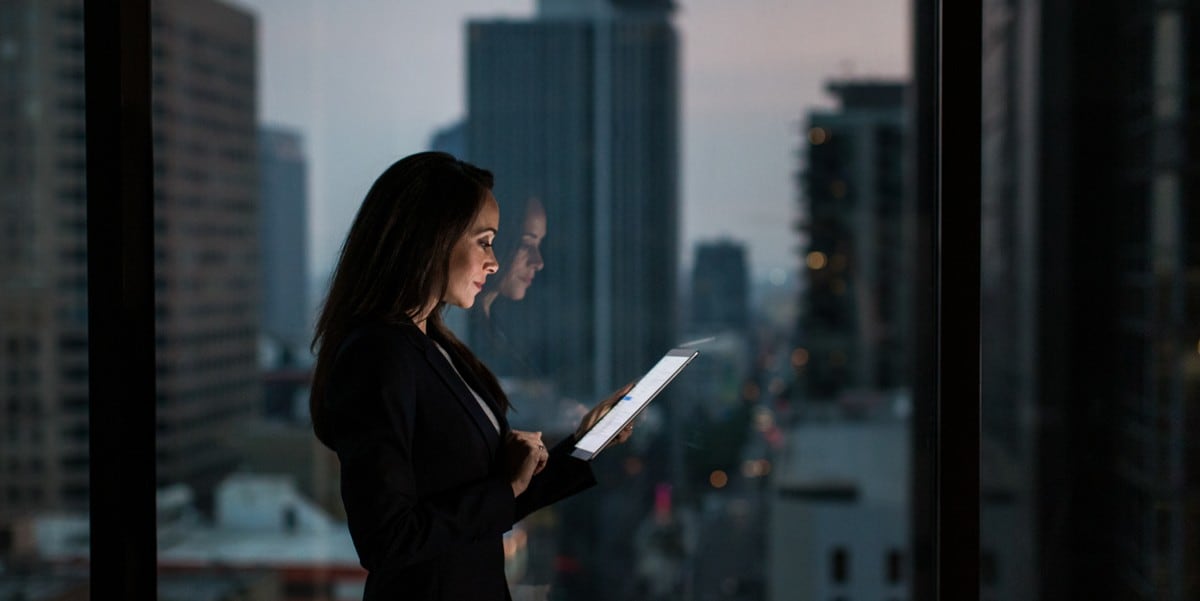 professional woman looking at phone, standing in front of window, skyscrapers in the background
