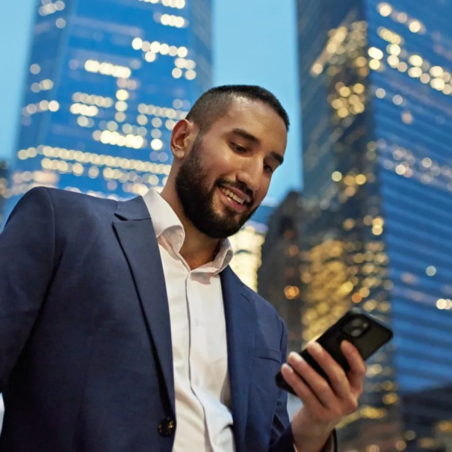 professional man looking at cell phone, skyscrapers behind him
